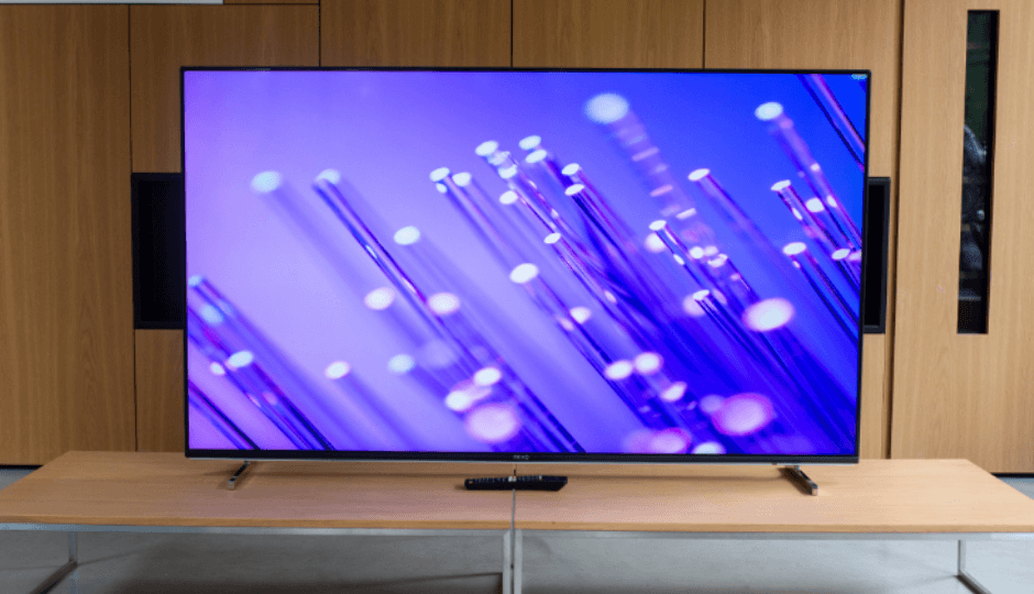 A PEAQ flatscreen with the remote control on a sideboard, in a meeting room with wooden walls 